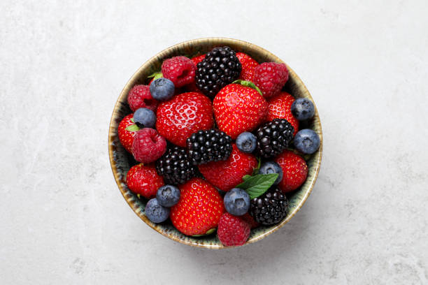 Different fresh ripe berries in bowl on light grey table, top view