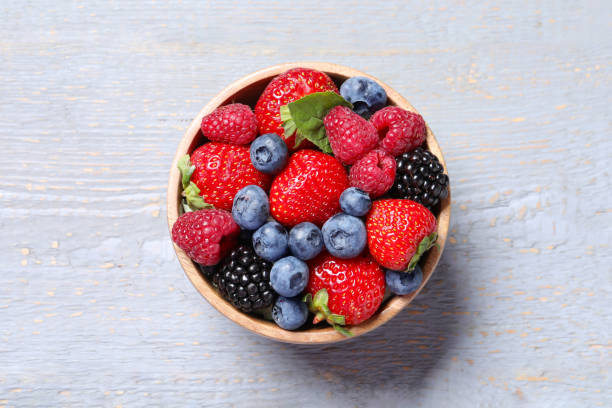 istock Different fresh ripe berries in bowl on light grey wooden table, top view 1945651395
