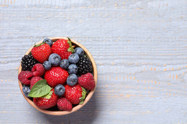 istock Different fresh ripe berries in bowl on light grey wooden table, top view. Space for text 1945651400