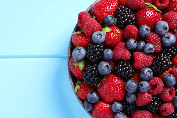 istock Different fresh ripe berries in bowl on light blue wooden table, top view. Space for text 1945652455