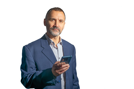 Madrid, Spain. Half-length view of a mature bearded man in a suit looking at the camera and holding a mobile phone, isolated against a white background