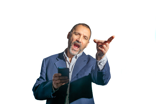 Madrid, Spain. Half-length view of an ecstatic, mature, bearded man in a suit looking at the camera, holding a mobile phone in one hand, and pointing forward with the other. Isolated against a white background.