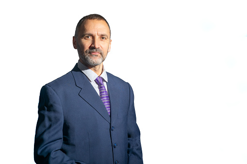 Madrid, Spain. Half-length view of a stylish and smiling mature bearded man in a suit and tie looking at the camera. Isolated against a white background.