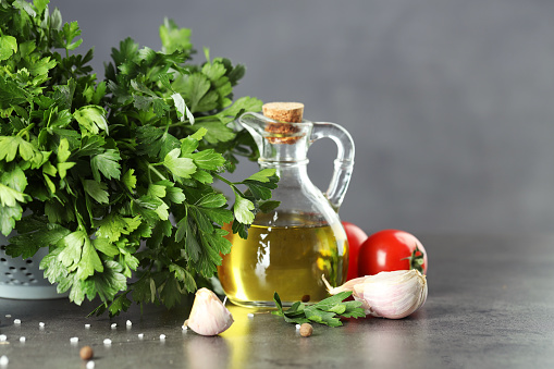 Fresh parsley, oil and other products on grey table, closeup. Space for text