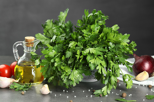 Fresh parsley, oil and other products on grey table