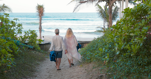 Mature couple walk down lush corridor to beach