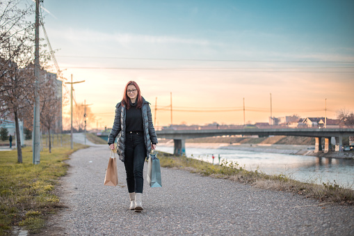 Young woman walking  next to river after shopping, she is holding bags in her hands