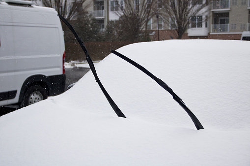 Preparing for heavy snow storm by lifting windshield wipers for easier cleaning of windshield.