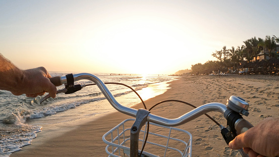 POV past bicycle handlebars to sunrise on beach and sea
