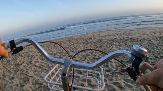 POV past bicycle handlebars to sunrise on beach and sea