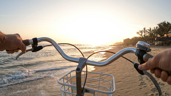 POV of hands pushing bicycle down beach at sunrise