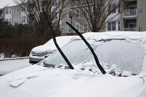 Preparing for heavy snow storm by lifting windshield wipers for easier cleaning of windshield.