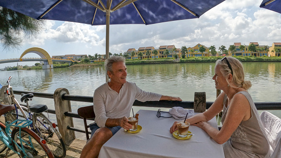 Mature couple enjoy beverage at outdoor cafe on riverbank