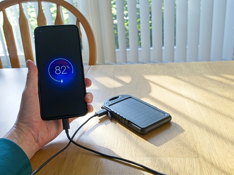 Smart phone being charged by an efficient solar powered battery bank in Melbourne, Florida - USA. Battery charging in a sunny Florida window, with cell phone being held in hand.