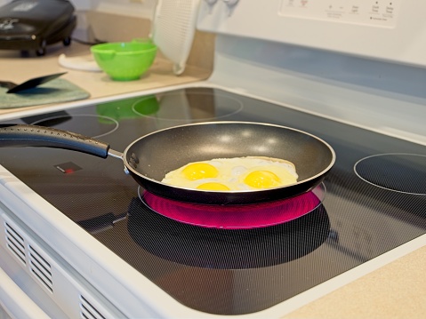 Cooking fried eggs at home on a ceramic top electric range in Melbourne, Florida - USA. Glowing red hot fast electric range with eggs frying in non-stick cookware. Florida galley kitchen with electric appliances.