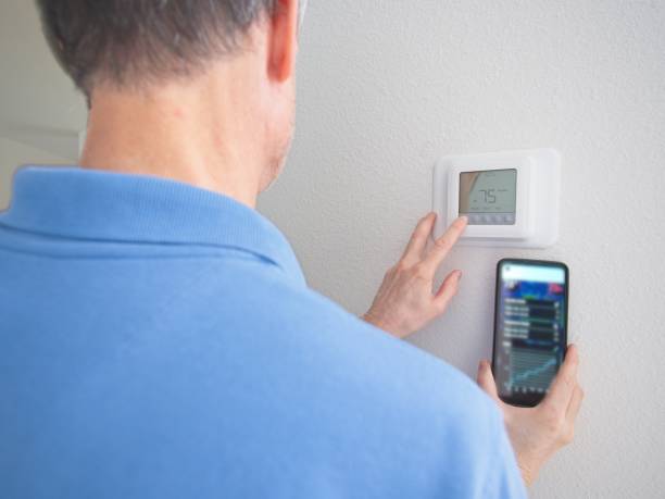 istock Home owner with back to the camera interacting with a smart thermostat and temperature sensor smart phone application in Melbourne, Florida - USA 1945804219
