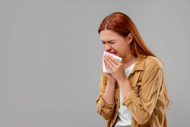 istock Suffering from allergy. Young woman with tissue sneezing on grey background, space for text 1945840430