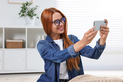 Happy young woman having video chat via smartphone at home