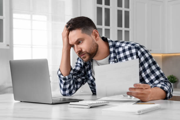 istock Man with laptop doing taxes at table in kitchen 1945875957