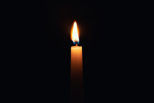 Candle burning in darkness over black background. Commemoration, necrology notice concept.