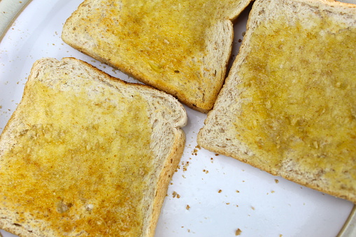 A photo of pieces of toast with butter on a white plate on a desk.