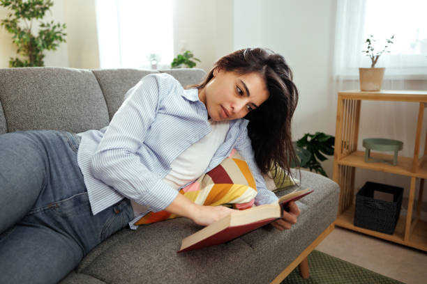 istock Young beautiful casually clothed woman reading book while relaxing on a sofa at home 1945917534