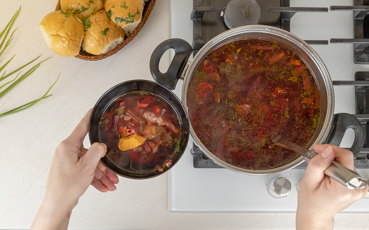 Women's hands pour Ukrainian borsch from a pot into a plate, top view