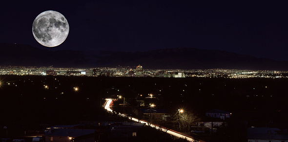 A night scene with city lights in the distance and a bright super full moon floats in the dark sky over Albuquerque, NM.