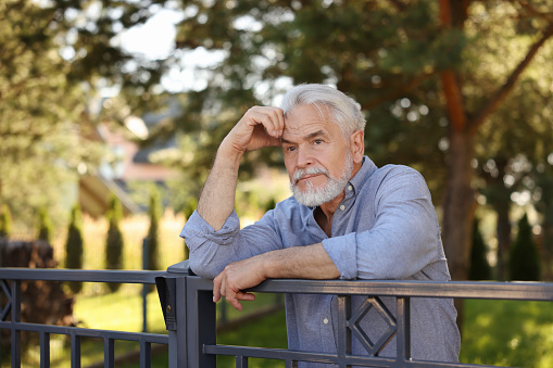 Portrait of serious senior neighbour leaning on fence outdoors