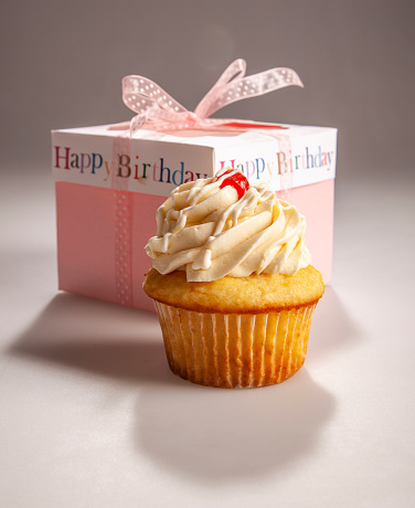 A gourmet cupcake with a Happy Birthday gift box. Vanilla cupcake with whipped vanilla frosting and topped with a cherry.