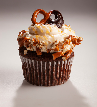 Gourmet chocolate cupcake with white buttercream frosting and a chocolate dipped\npretzel on top of the icing.