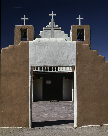 Entrance to the San Geronimo de Taos Catholic Chapel. The brown and white stucco is accented by the bright blue New Mexico sky. The church has with stood time as to mirror the strength of the Puebloan people adapting to the cultural changes over generations.