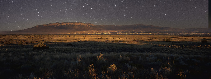 The stars are out at night in southern New Mexico. As the sun sets the base of the mountain range is illuminated.