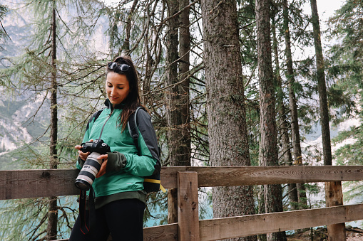 female photographer in Dolomites forest, north Italy, capturing the beautiful nature, trees, lakes and mountains with her mirrorless or DSLR camera.