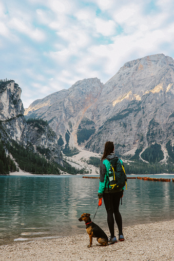 female hiker enjoys the beautiful outdoors in Dolomites, Italy. She is relaxing in the early morning next to Lago di Braies with her pet dog.