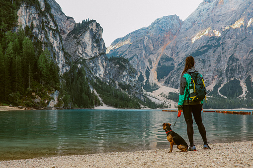 female hiker enjoys the beautiful outdoors in Dolomites, Italy. She is relaxing in the early morning next to Lago di Braies with her pet dog.