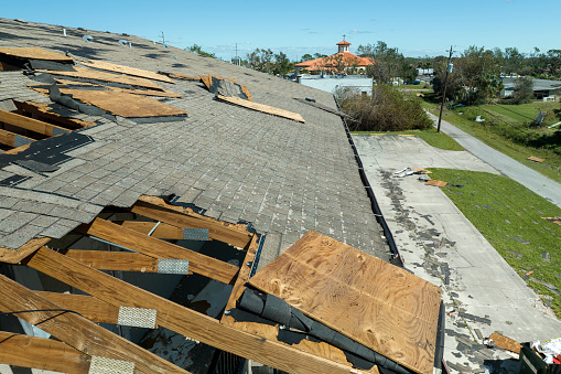 Consequences of natural disaster. Damaged house roof with missing shingles after hurricane Ian in Florida.