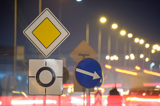 Roundabout road signs with blurred cars on city street traffic at night. Urban transportation concept.