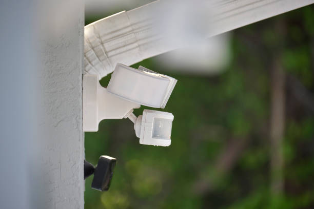 Motion sensor with light detector mounted on exterior wall of private house as part of security system.