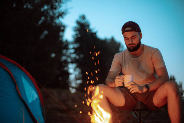 istock Young hiker man sitting next to camp fire and drinking coffee 1946164439