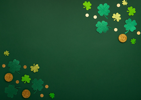 St Patricks day card with traditional symbols for irish party. Golden horseshoe, gold coins, clover leaves, green shamrocks on green background. Top view, copy space. St. Patrick's Day celebration concept.