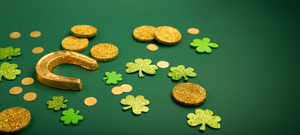 St Patricks day card with traditional symbols for irish party. Golden horseshoe, gold coins, clover leaves, green shamrocks on green background, copy space. St. Patrick's Day celebration concept.