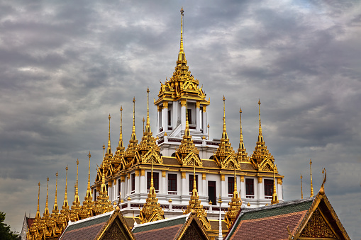 Metal Temple (Wat Ratchanatdaram) in Bangkok, Thailand. Metal spires on roof. Dark cloudy sky overhead