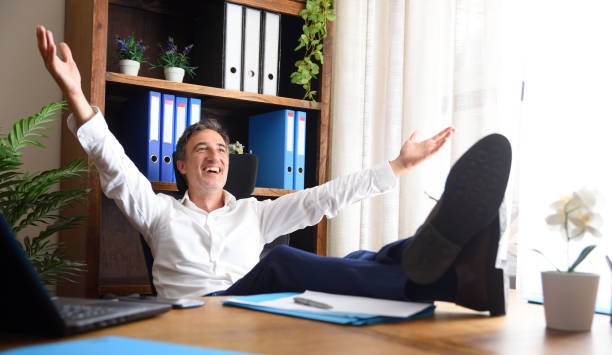 istock Happy man with open arms sitting with feet on table 1946264894