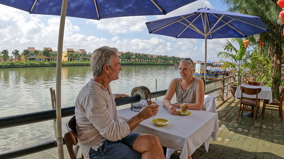 Mature couple enjoy beverage at outdoor cafe on riverbank