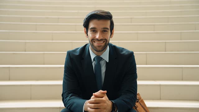 Smiling skilled businessman looking at camera while sitting on stairs. Exultant.