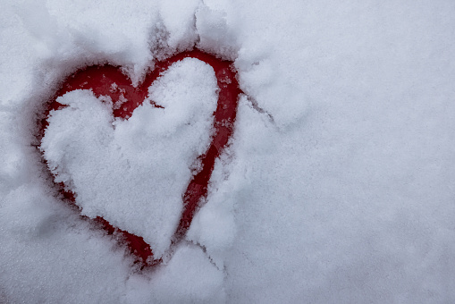 Hand drawn heart on the top of a red car covered with fresh white snow