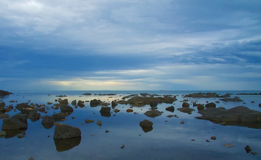 Black rocks in shallow water at a beach in Australia against a blue and cloudy sky