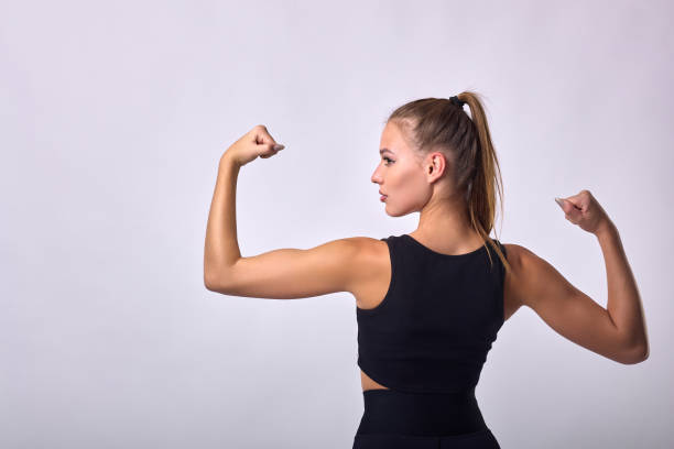 Young athlete in black uniform stands with back to hands, showing pumped biceps