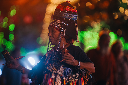 Bangkok, Thailand - January 12, 2024:\nA Thai street vendor sells traditional northern hats, handmade bracelets and necklaces as she strolls along bustling Khao San Road at night.